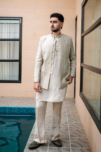 Light sage/grey prince coat with vertical embroidery and mirror work all over. Band collar with subtle gold detailing. Paired with matching kurta pajama