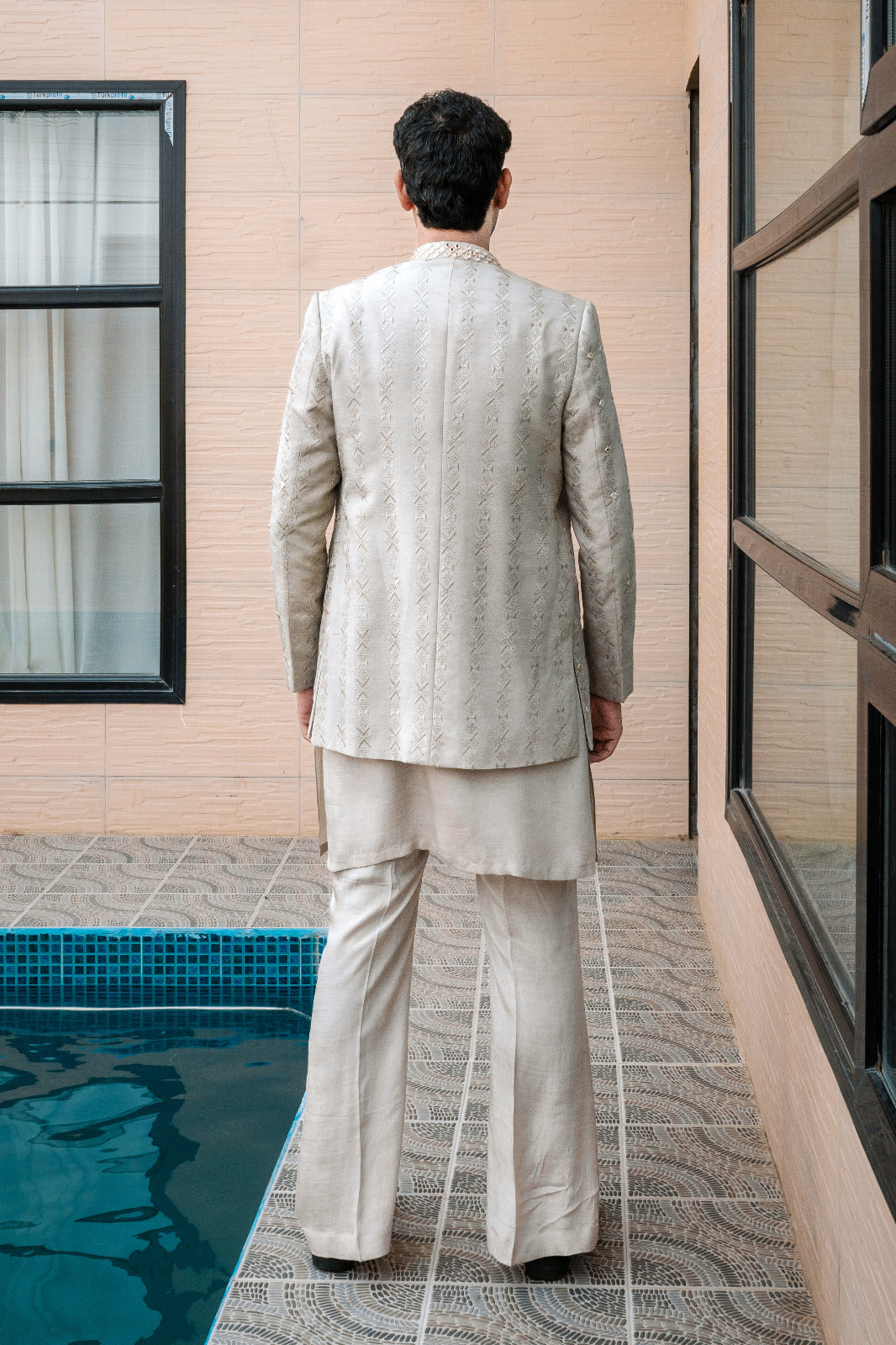 Light sage/grey prince coat with vertical embroidery and mirror work all over. Band collar with subtle gold detailing. Paired with matching kurta pajama